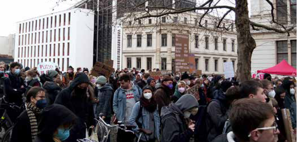 Studenten stehen mit Bannern zusammen. Viele tragen einen Maske. 