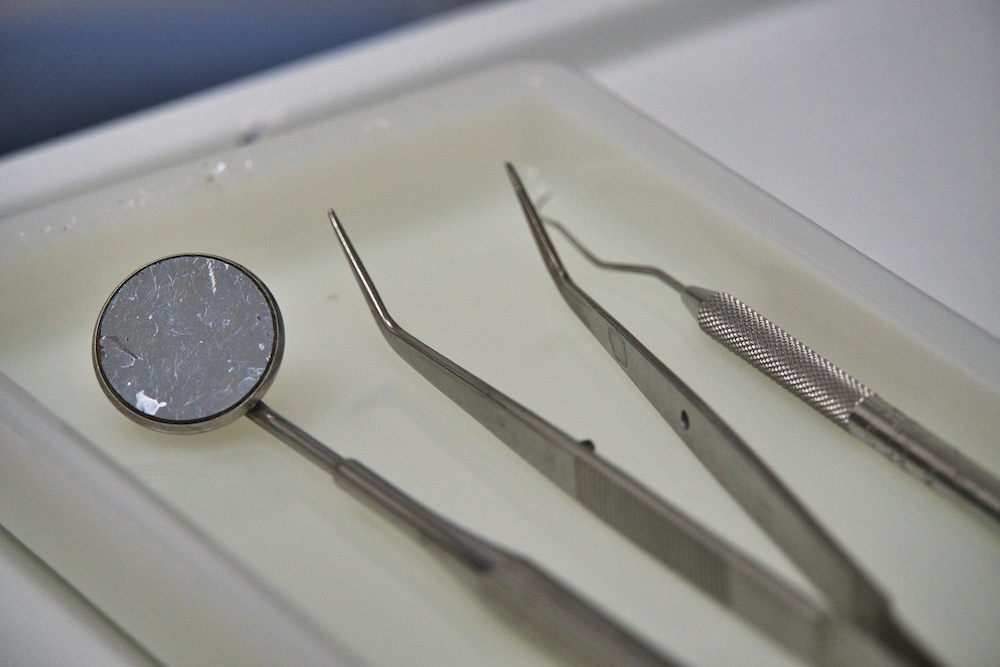 Auf dem Bild ist ein weißes Tablett mit Zahnarztwerkzeug, z. B. einem Zanharztspiele und einer Art Pinzette zu sehen.