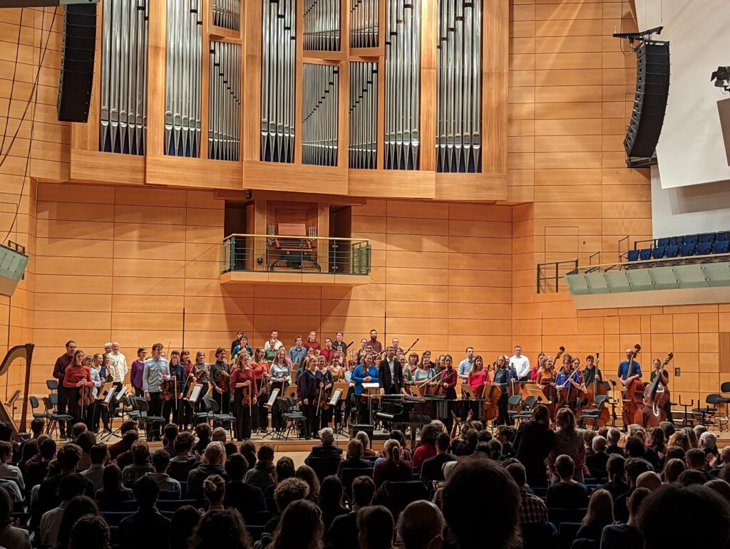 Blick über die Köpfe des Publikums auf das akademische Orchester. Im Hintergrund die Orgel.