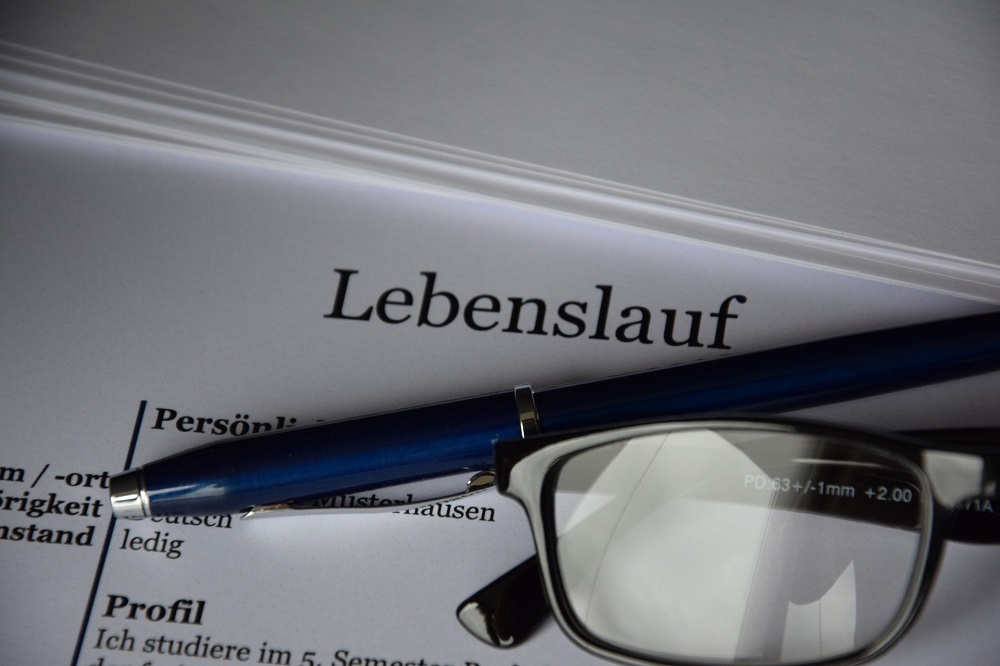 Pictured is a pair of glasses and a pencil lying on a resume document.